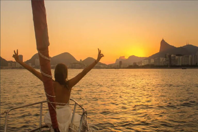 Chica posando en un velero blanco navegando por la Bahía de Guanabara en Río de Janeiro durante un atardecer dorado.