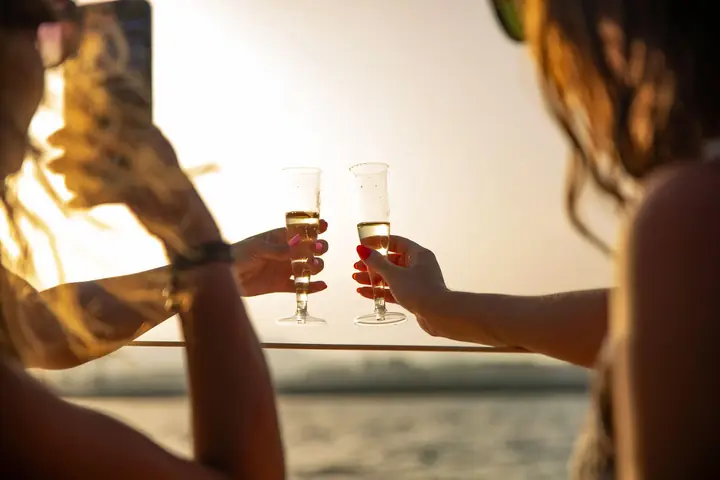 Twee gasten die bij zonsondergang op een catamarandek met cava toasten bij Alicante