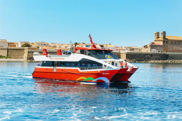 Rood glasdekkerbootje aankomt op het eiland Tabarca, met de oude muren en de kerk achteraan