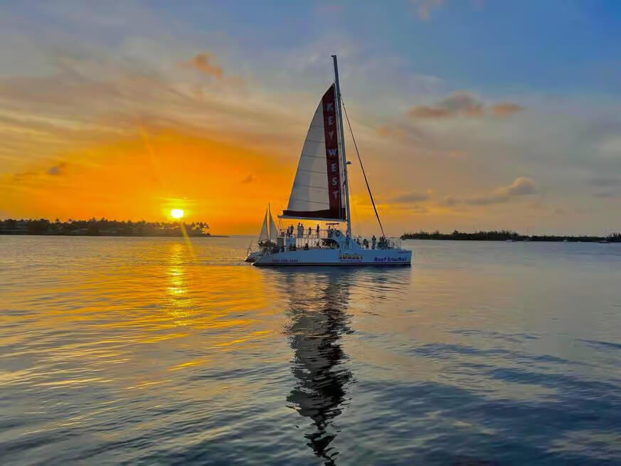 A large catamaran sailing at sunset in Key West with passengers on deck.